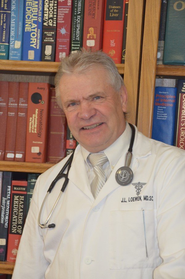 Dr. John L. Loewen in his white coat in front of a shelf of medical books